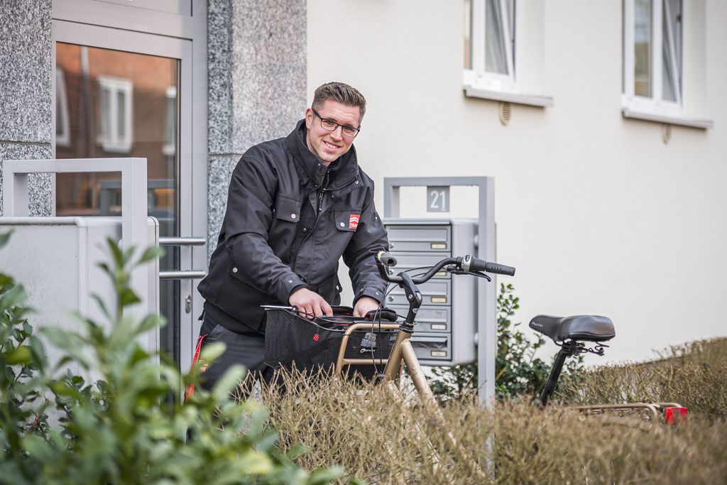 Ein TRAVE-Hauswart legt etwas in seinen Fahhradkorb und lächselt in die Kamera.