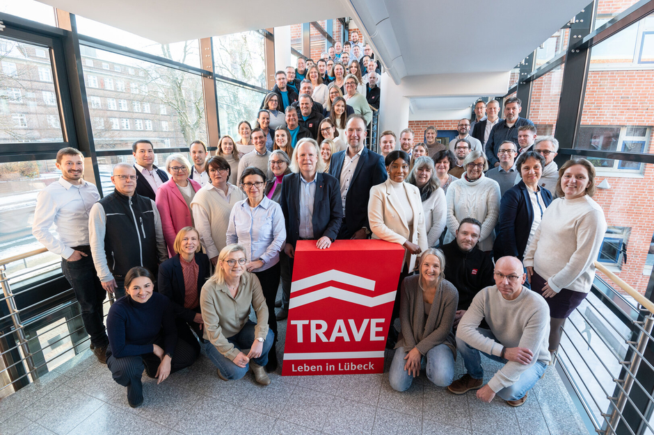 Das TRAVE-Team im Treppenhaus der Falkenstraße 10. Im Vordergrund das TRAVE-Logo und die Geschäftsführer Dr. Matthias Rasch und Sebastian Weist.