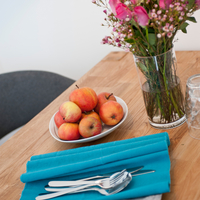 Tisch mit Platzdeckchen und Besteck, Äpfel in einer Schale, Vase mit Blumen.