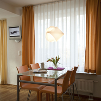 Der Esstisch mit vier Stühlen steht vor dem Fenster. Im Hintergrund der Fernseher an der Wand.