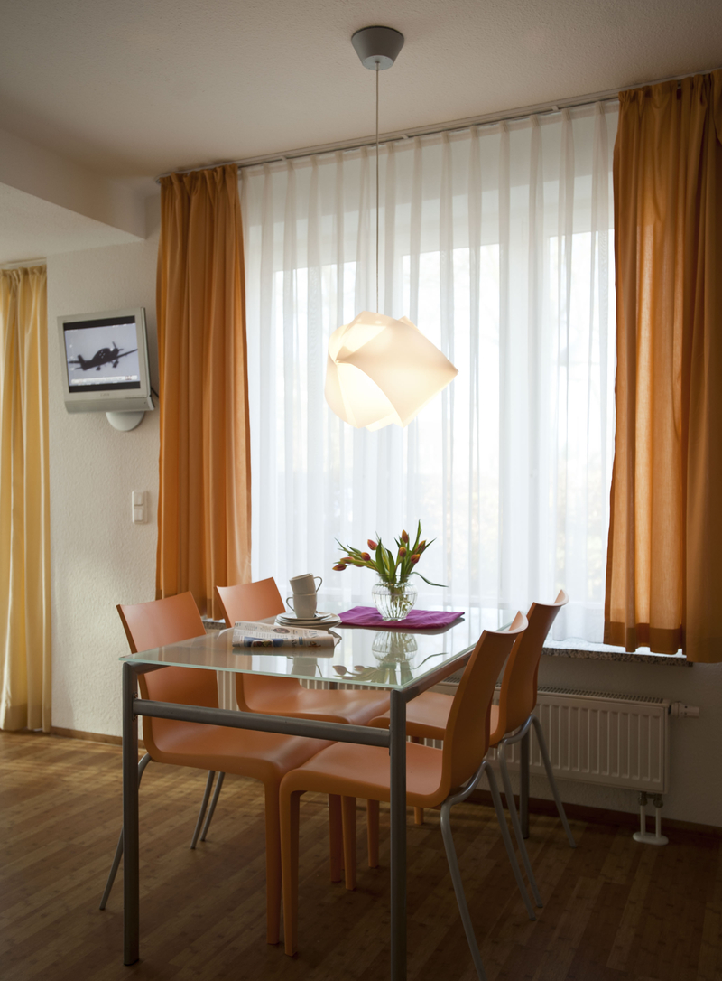 Der Esstisch mit vier Stühlen steht vor dem Fenster. Im Hintergrund der Fernseher an der Wand.
