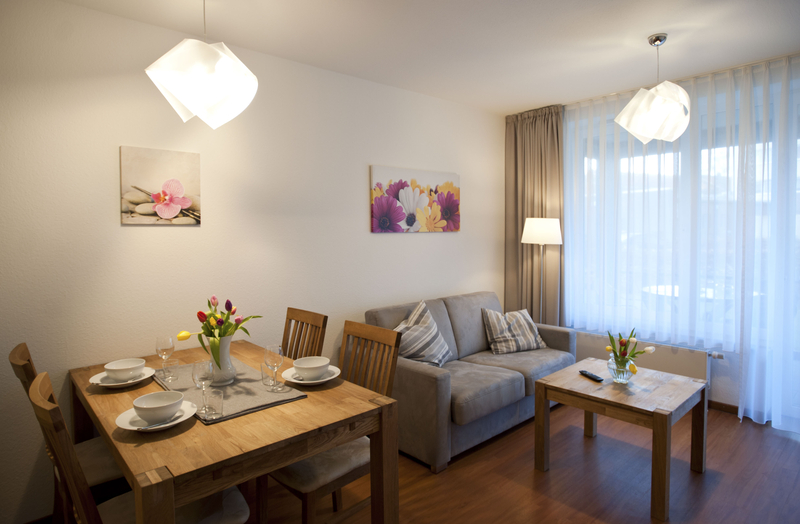 Das Wohnzimmer mit gemütlicher Couch Couchtisch aus Holz. Auch der Esstisch und die vier Stühlen sind aus Holz.