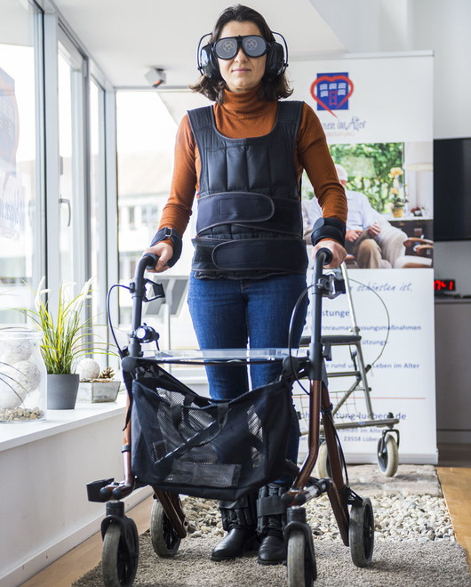Person im Anzug zur Alterssimulation testet mit einem Rollator den Parcours. Person im Anzug zur Alterssimulation testet mit einem Rollator den Parcours.