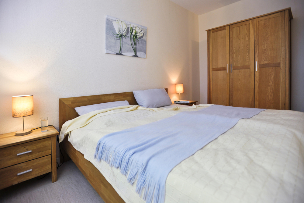 Blick ins Schlafzimmer mit Doppelbett, Nachtschränken und einem großen Kleiderschrank aus Holz.