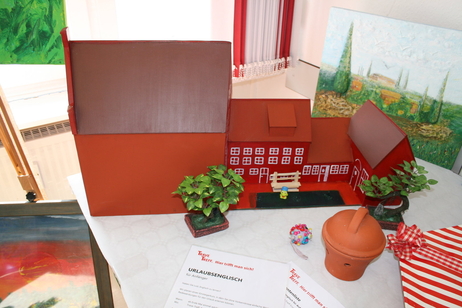 Das Modell von einem Haus steht auf einem Tisch zusammen mit weiteren Gegenständen. Davor liegt ein Monatsplan mit Aktivitäten im Trave-Treff.