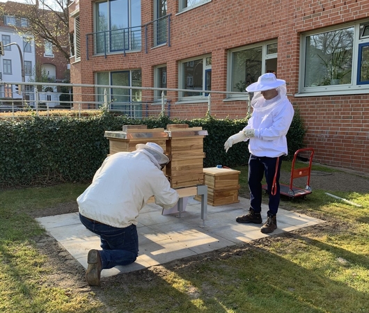 Der TRAVE-Imker und der Auszubildende im Imkerbekleidung vor dem Bienenstock.