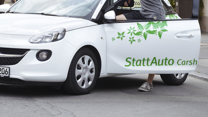 Zwei Menschen unterhalten sich gut gelaunt an einem Carsharing-Auto von StattAuto. 