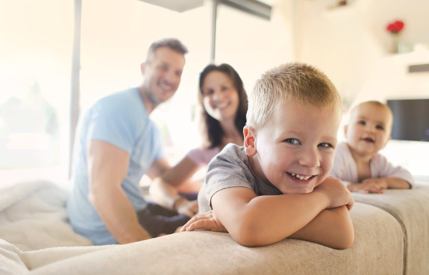 Eine fröhliche Familie. Der ältere Junge, ca. 4 Jahre alt, lächelt verschmitzt in die Kamera. Im Hintergrund die Eltern und ein Baby.