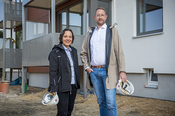 Zwei Mitarbeitende der TRAVE mit Bauhelmen vor einem Wohngebäude im Bau